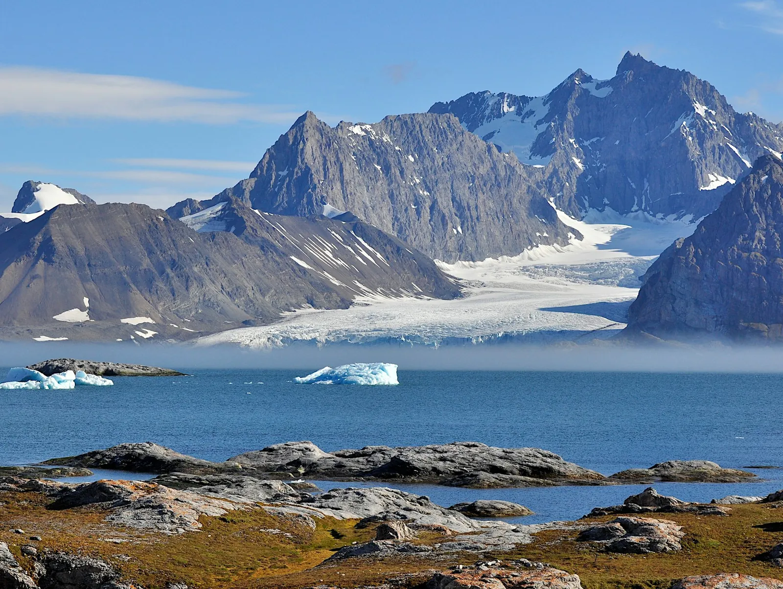 A glacier meeting the sea between snow-covered peaks in the high Arctic.
