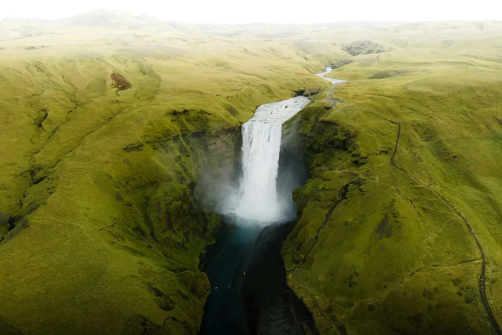 An aerial view of a waterfall cutting through the green moss-covered Icelandic highlands.