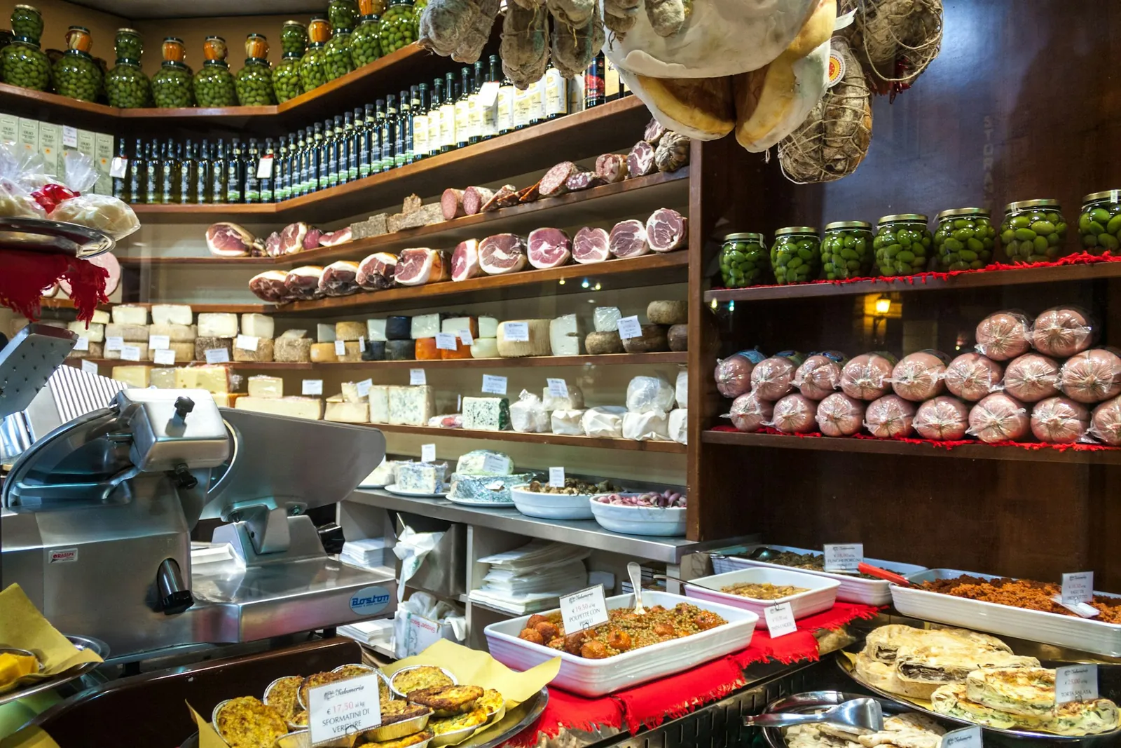 An Italian deli counter hung with prosciutto, its cases full of cheese and prepared dishes.